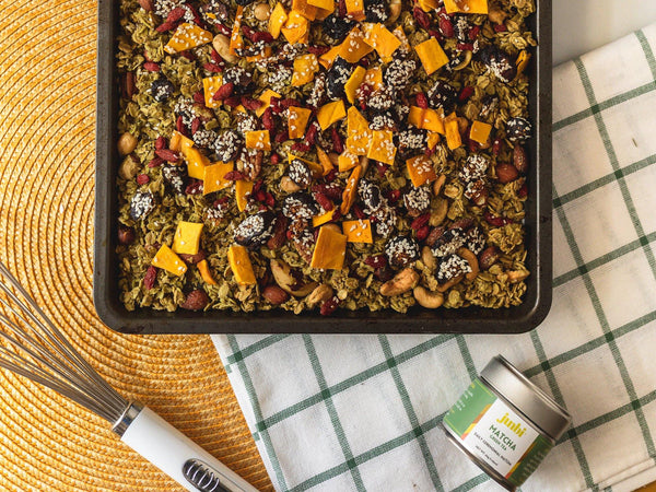 A square pan of Amazebowls' Matcha Granola using Junbi with dried mango on top. A Junbi matcha tin lays next to the square pan.